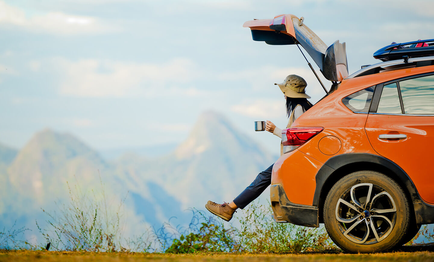 Person with coffee near an open vehicle trunk, suggesting lifestyle and budgeting.